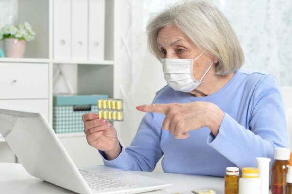 ill beautiful senior woman with facial mask holding pills