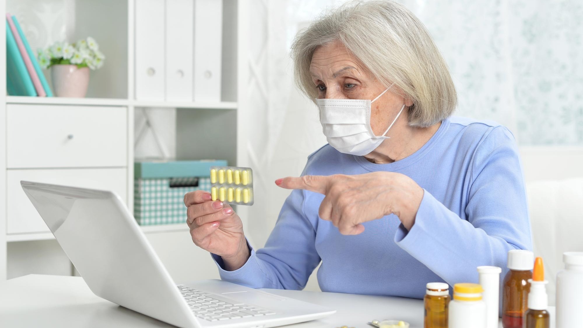 ill beautiful senior woman with facial mask holding pills