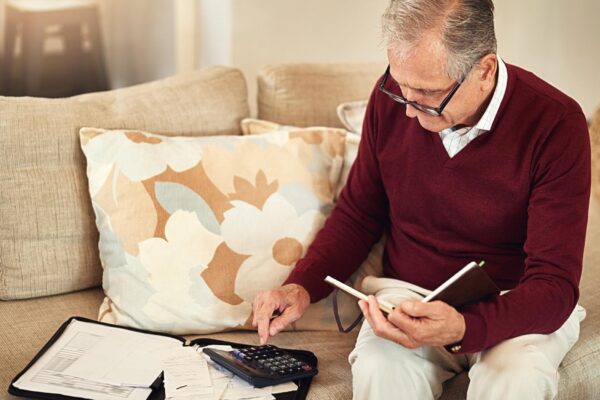 Senior man notebook and calculator on sofa for budget planning and savings account for retirement Elderly person bills and couch in lounge for mortgage personal debt and loan repayment ay home
