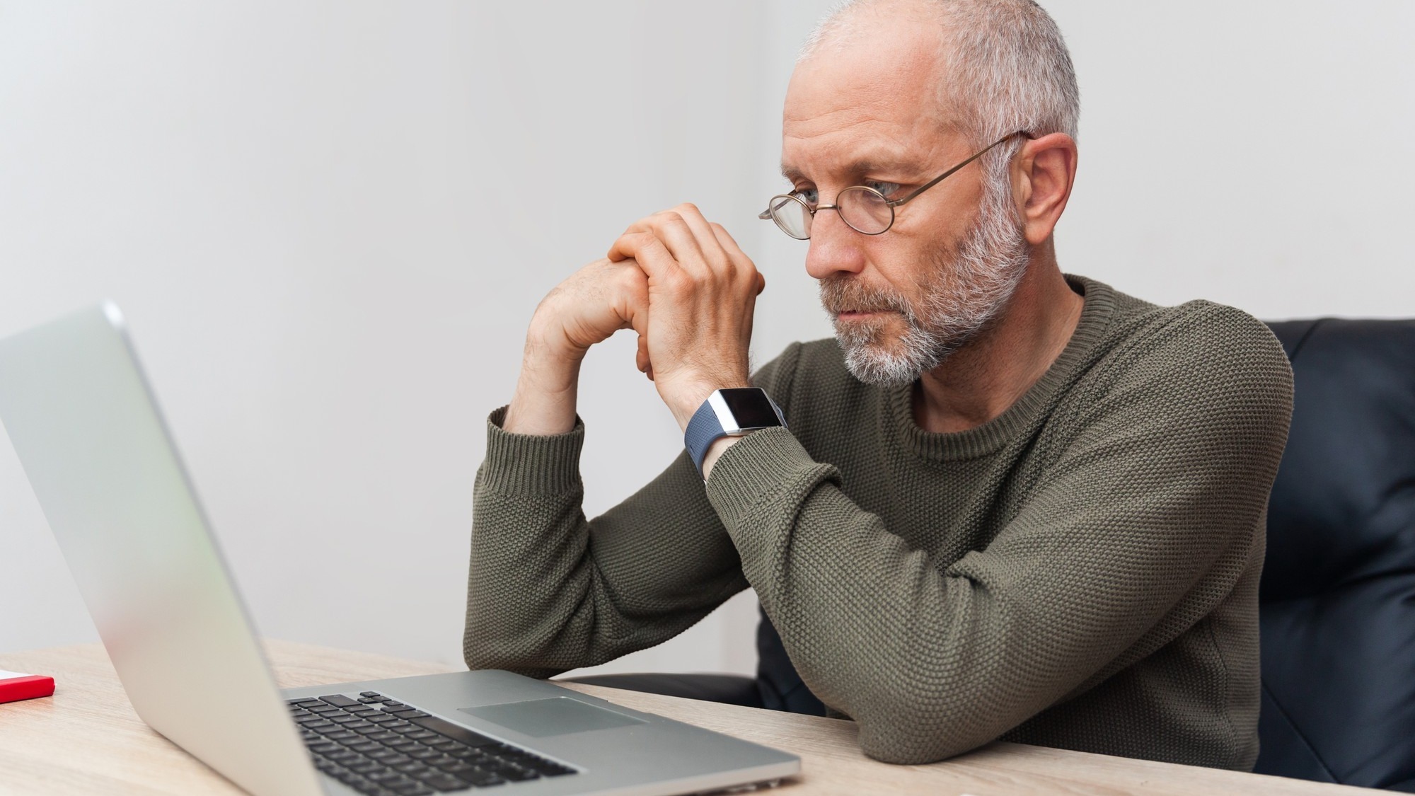 Adult, pensive man with gray hair working on laptop