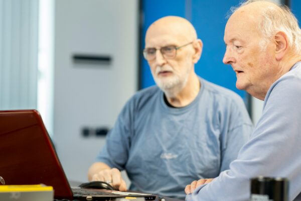 two men sitting at a table looking at a laptop