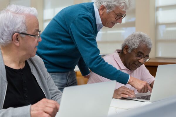 Three senior adults collaborating in a classroom setting on laptops, focusing on technology learning.