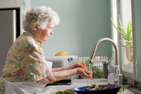 woman wearing yellow and pink floral dress wahing carrots