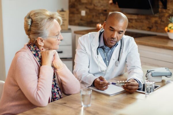 African American doctor talking about medicines with mature woman during home visit