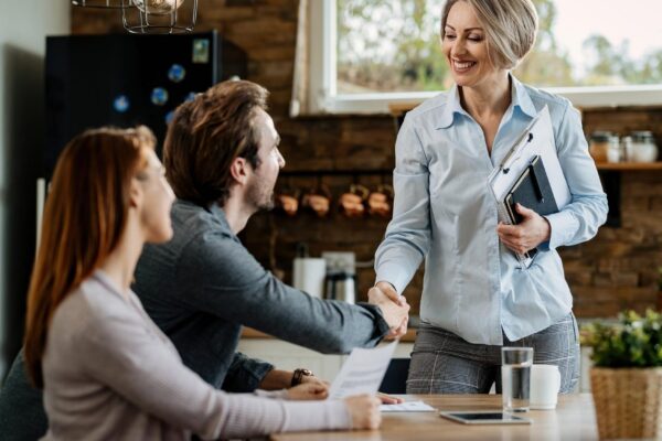 Happy insurance agent meeting with young couple and shaking hands with a man at their home