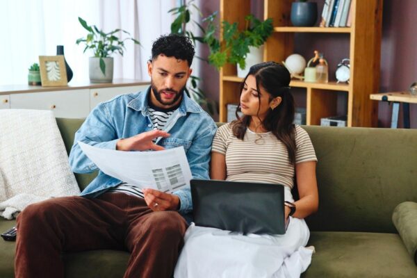 Documents laptop and couple on sofa in home for bills payment receipts and banking Marriage relationship and man and woman with paperwork for financial planning with taxes insurance and budget