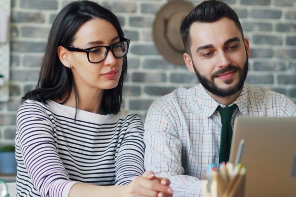 a man and woman sitting at a table looking at a laptop