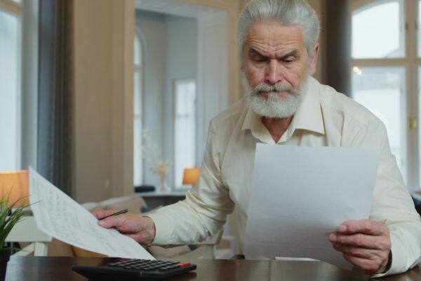 Serious mature man calculating bills, checking finances manage personal finances seated at table at home.