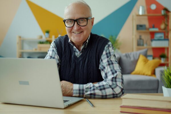 Smiling elderly man with glasses at laptop computer.