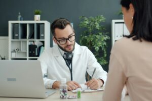 Doctor writing notes while patient sits opposite.