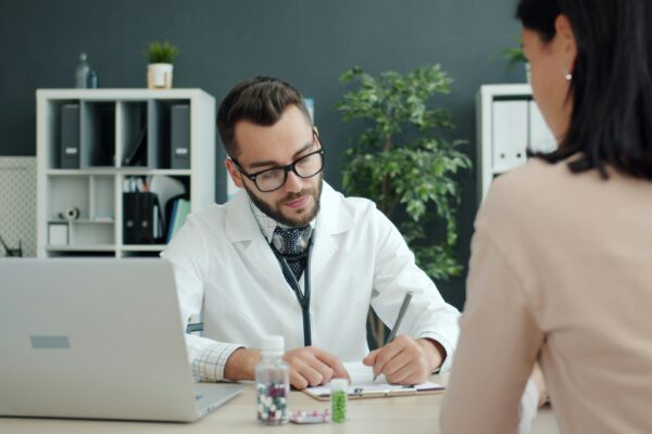 Doctor writing notes while patient sits opposite.