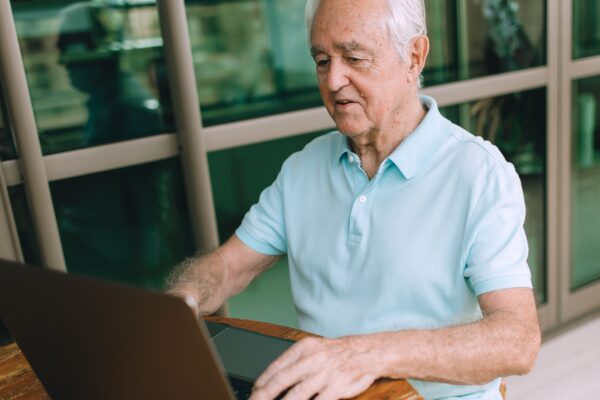 Elderly man enjoying technology, typing on laptop indoors.