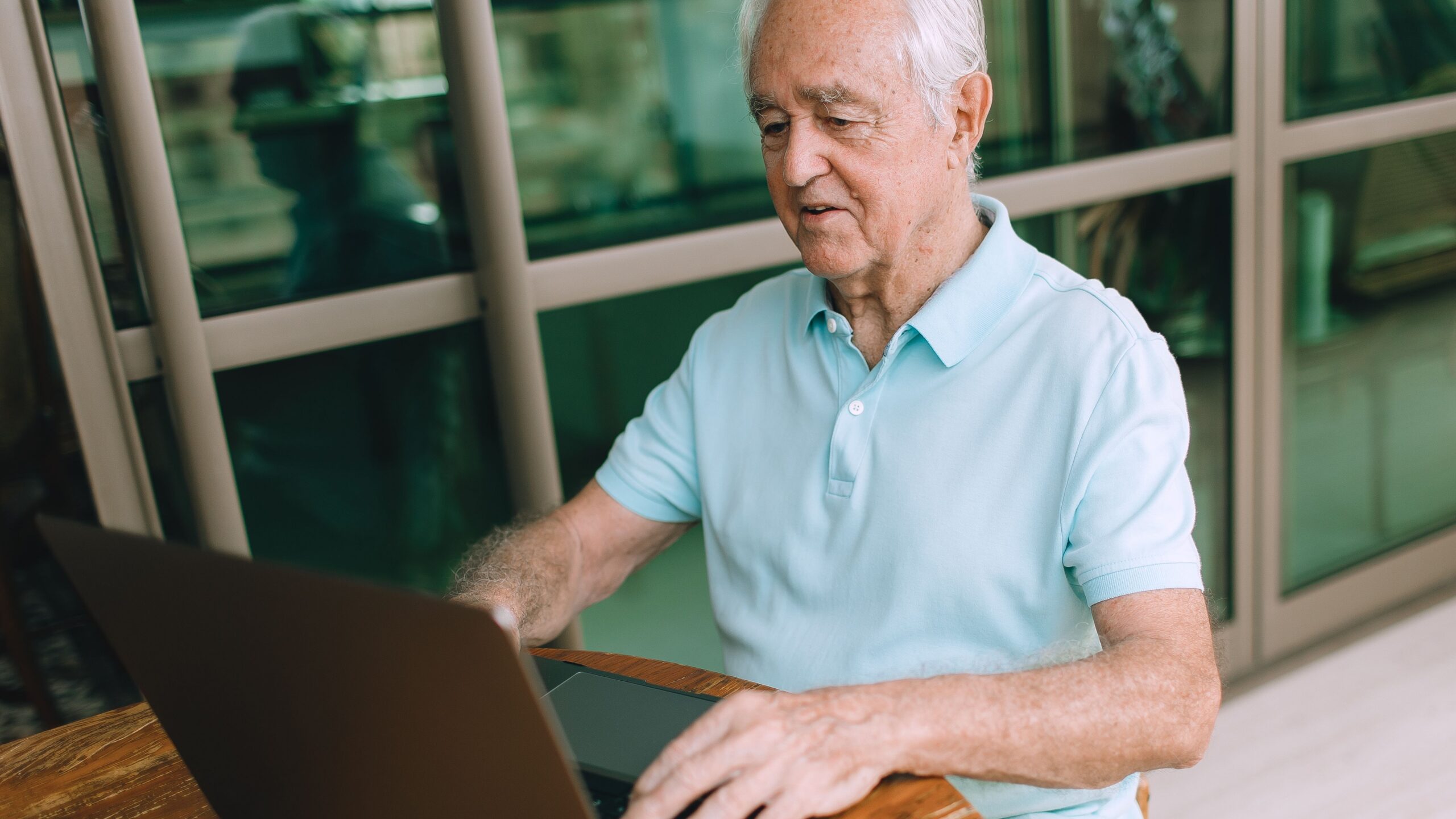 Elderly man enjoying technology, typing on laptop indoors.