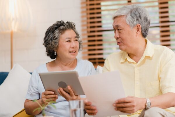 Asian elderly couple using tablet watching TV in living room at home, couple enjoy love moment while lying on sofa when relaxed at home.