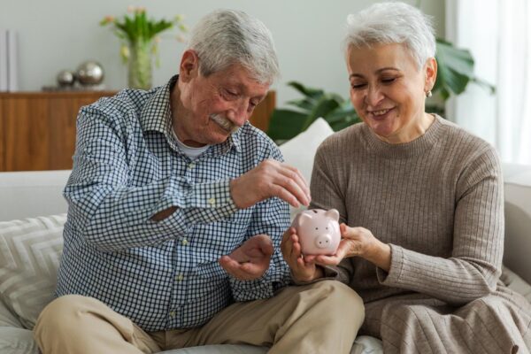 Saving money investment for future senior adult mature couple holding piggy bank putting money coin