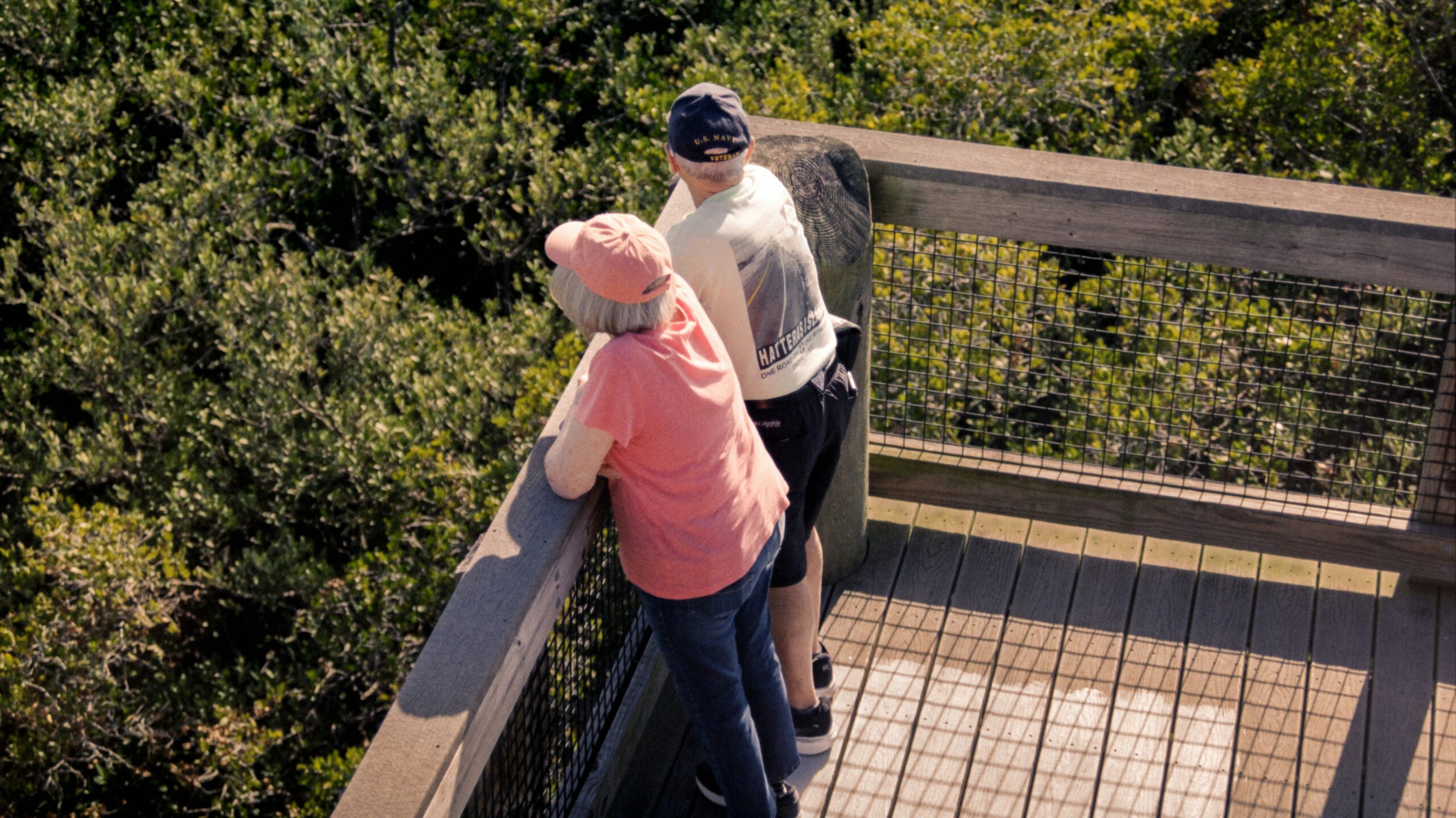 Two people on a wooden observation deck overlooking trees