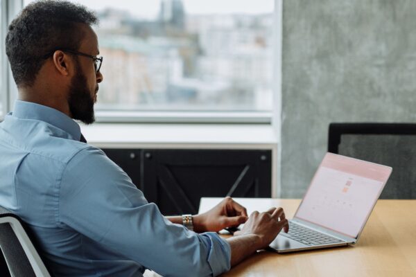 Black man working on laptop in modern office with city view, focused on technology and productivity.