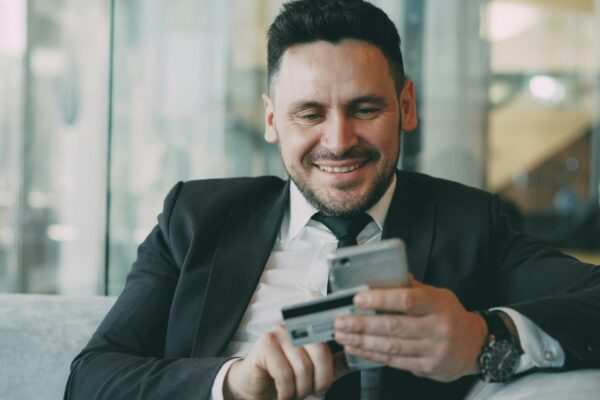 Man in suit smiling while holding phone and credit card