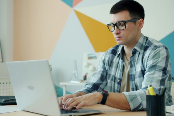 Man wearing glasses types on a laptop at a desk.