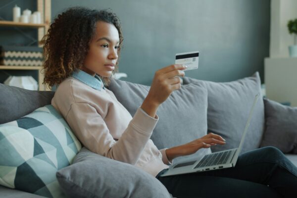 Woman using laptop and credit card on sofa