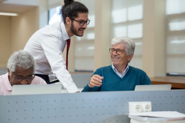 A classroom scene in Portugal where seniors learn computer skills from a young instructor. Engaged and smiling.