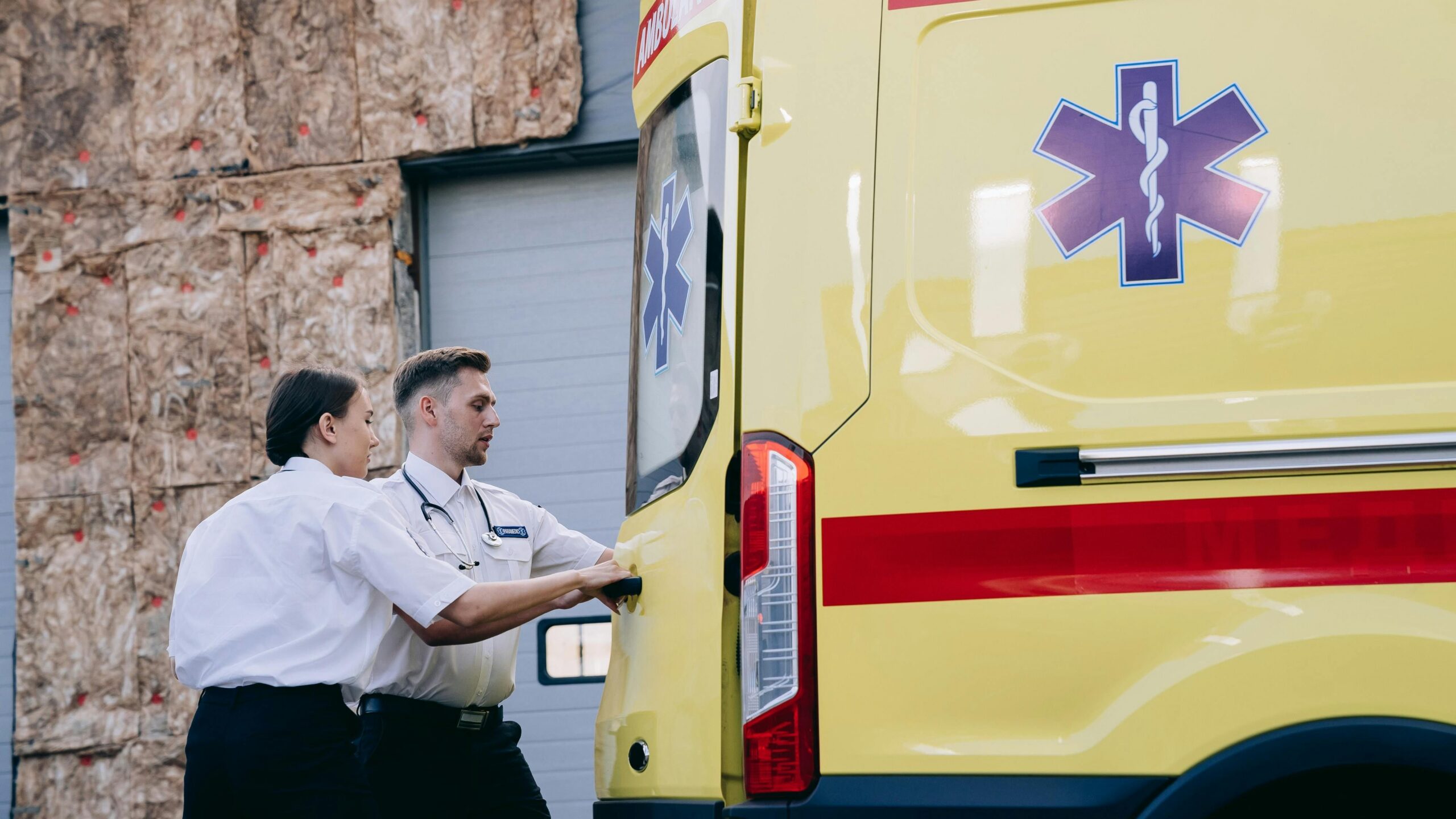 Two paramedics close the rear doors of an ambulance, preparing for emergency response.
