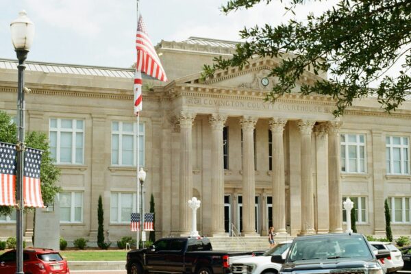 Classical building with columns, american flags, and parked cars.