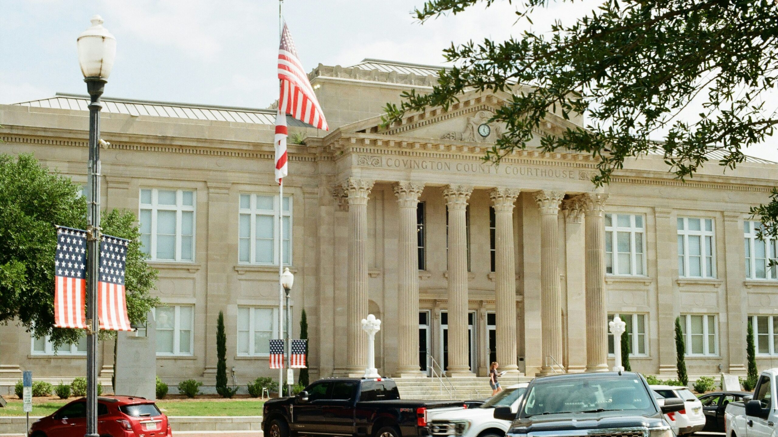 Classical building with columns, american flags, and parked cars.