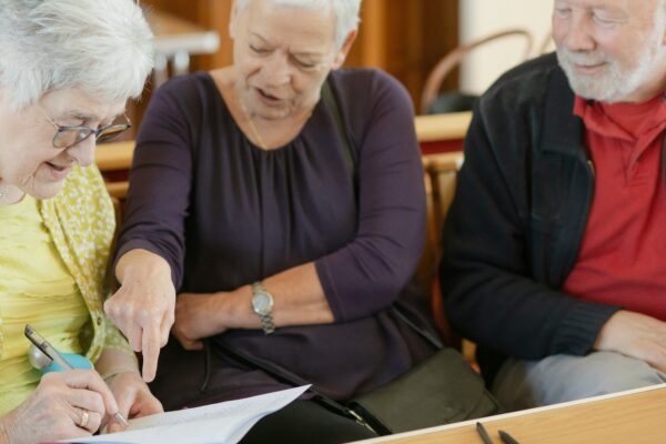 Three older adults are looking at a paper.