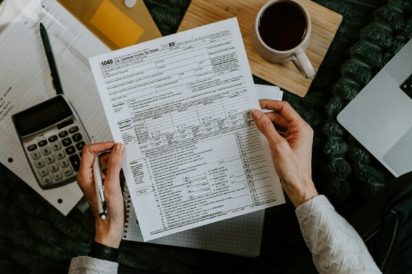Hands holding tax forms with calculator and laptop.
