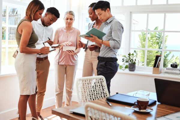 Business coach startup team workshop and mature business woman coaching men and women in modern office Diversity teamwork and writing note on strategy and planning advice from mentor or consultant