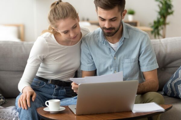 Young serious couple reading financial documents checking bills with laptop