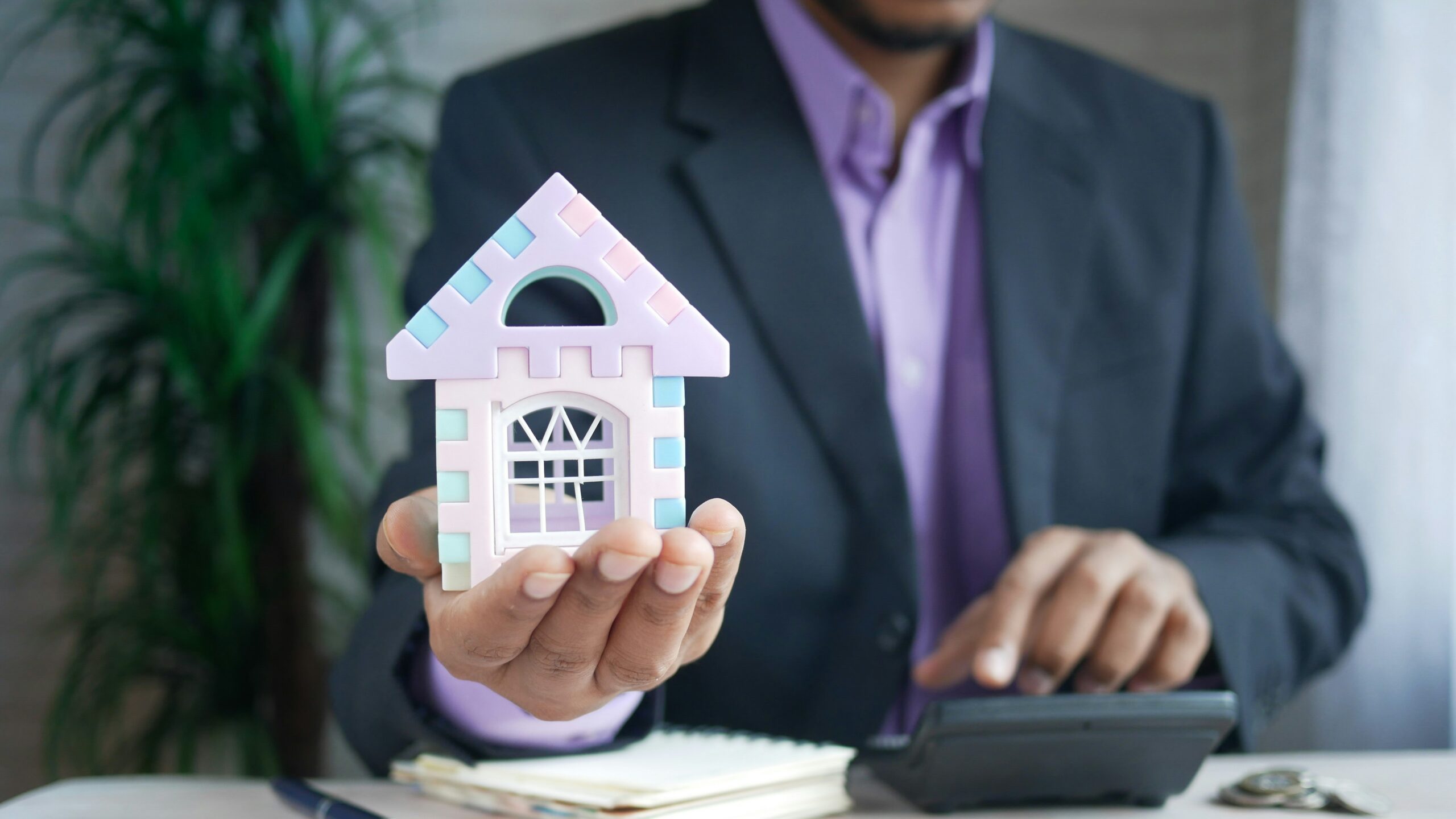 man holding model house at desk with calculator