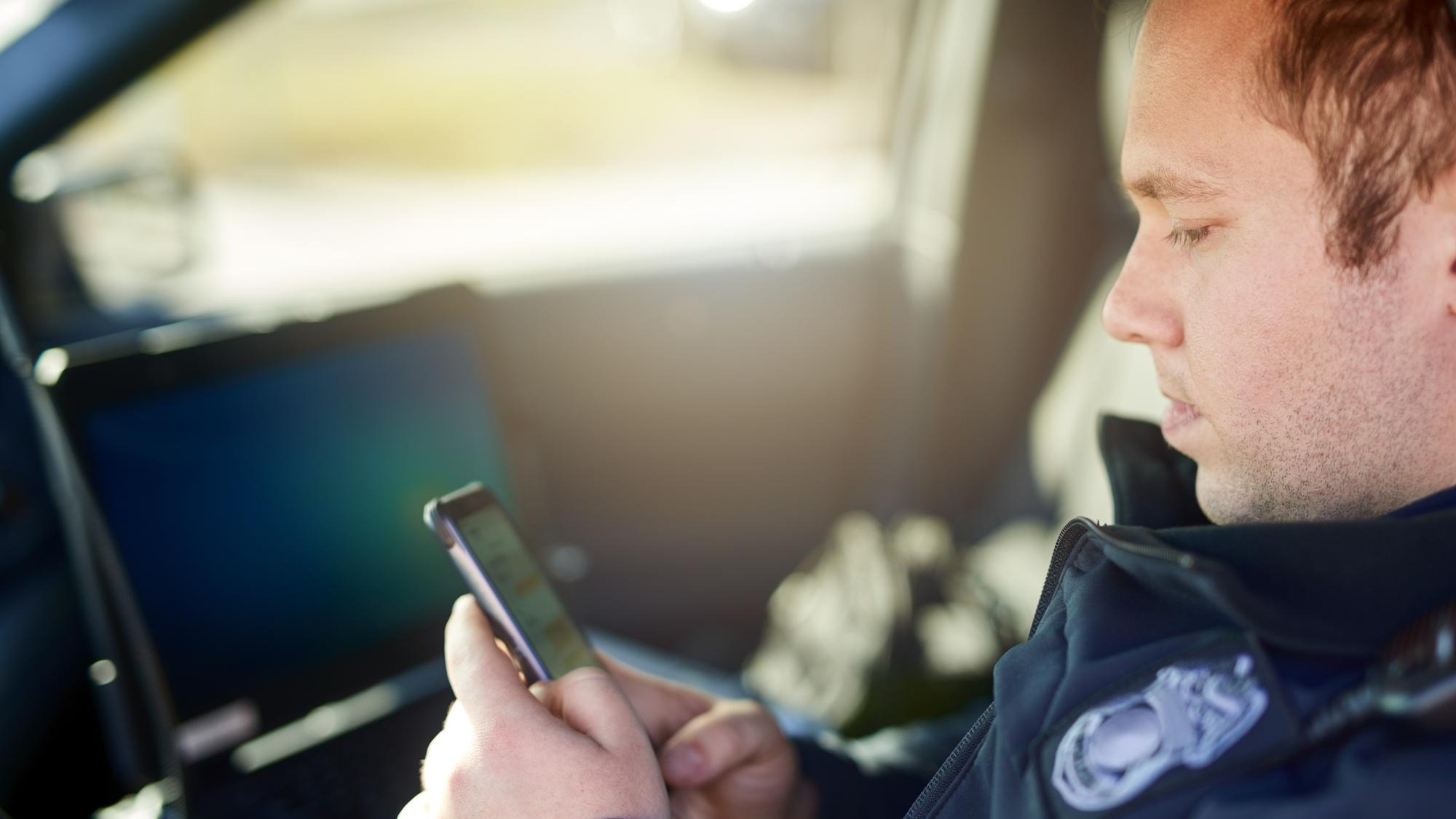 Police officer and man texting with phone in patrol car for security contact law enforcement update and mobile notification Policeman typing message on cellphone for crime news connection and app
