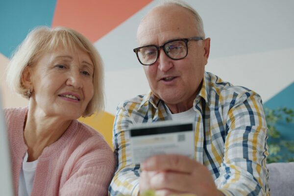 Elderly couple looking at credit card and laptop.