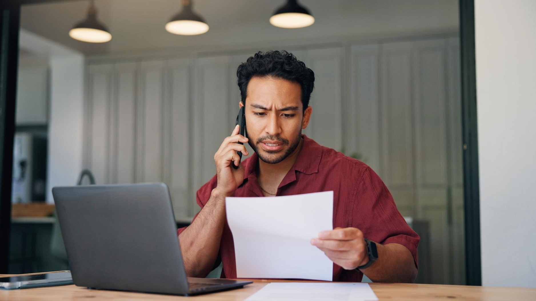 Laptop documents and businessman with phone call in office with contact for programming mistake Computer confused and web developer on mobile discussion for feedback on coding error with paperwork