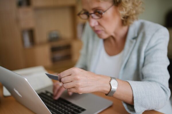 Woman with glasses sitting at her office table, holding a plastic card and typing on the laptop.
