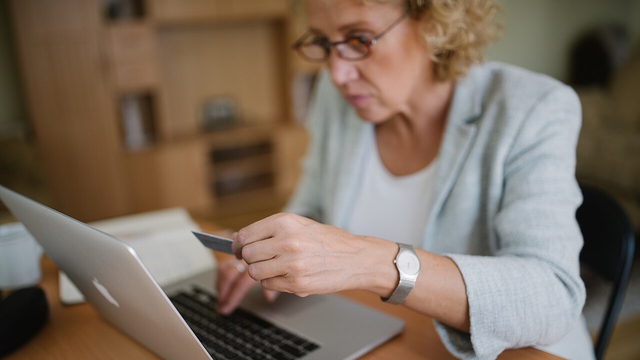 Woman with glasses sitting at her office table, holding a plastic card and typing on the laptop.
