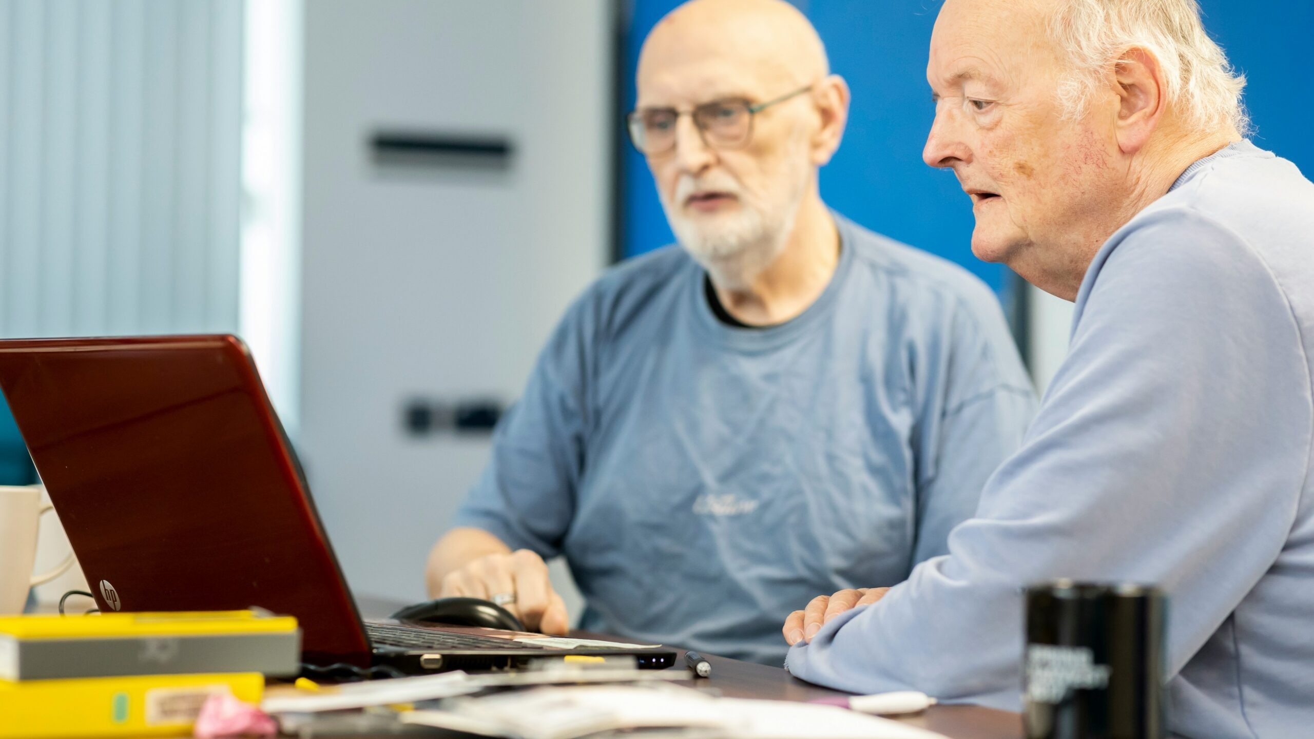 two men sitting at a table looking at a laptop