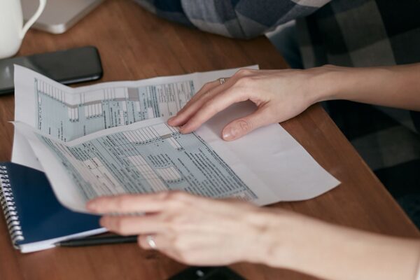 Close-up of hands organizing tax forms on a desk with a calculator, laptop, and notebook.