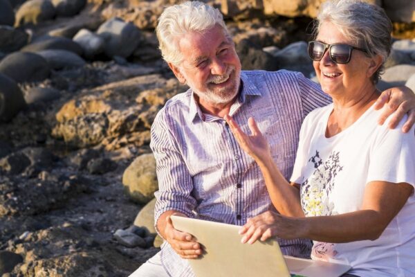Cheerful couple using laptop while sitting at beach