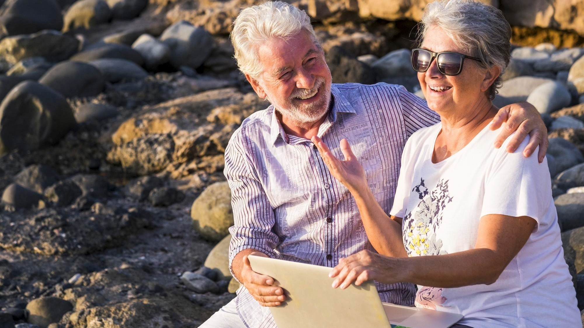 Cheerful couple using laptop while sitting at beach
