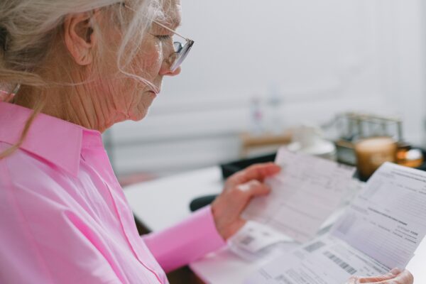 Elderly woman in a pink shirt reviewing paperwork at home.