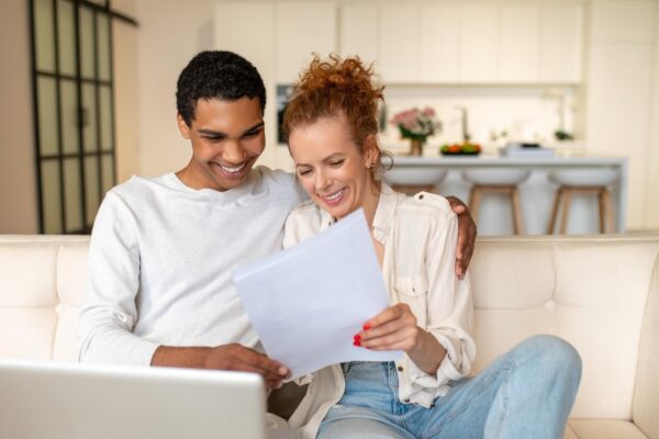 Surfing internet. Young man with a laptop sitting on the sofa, his wife standing next to him