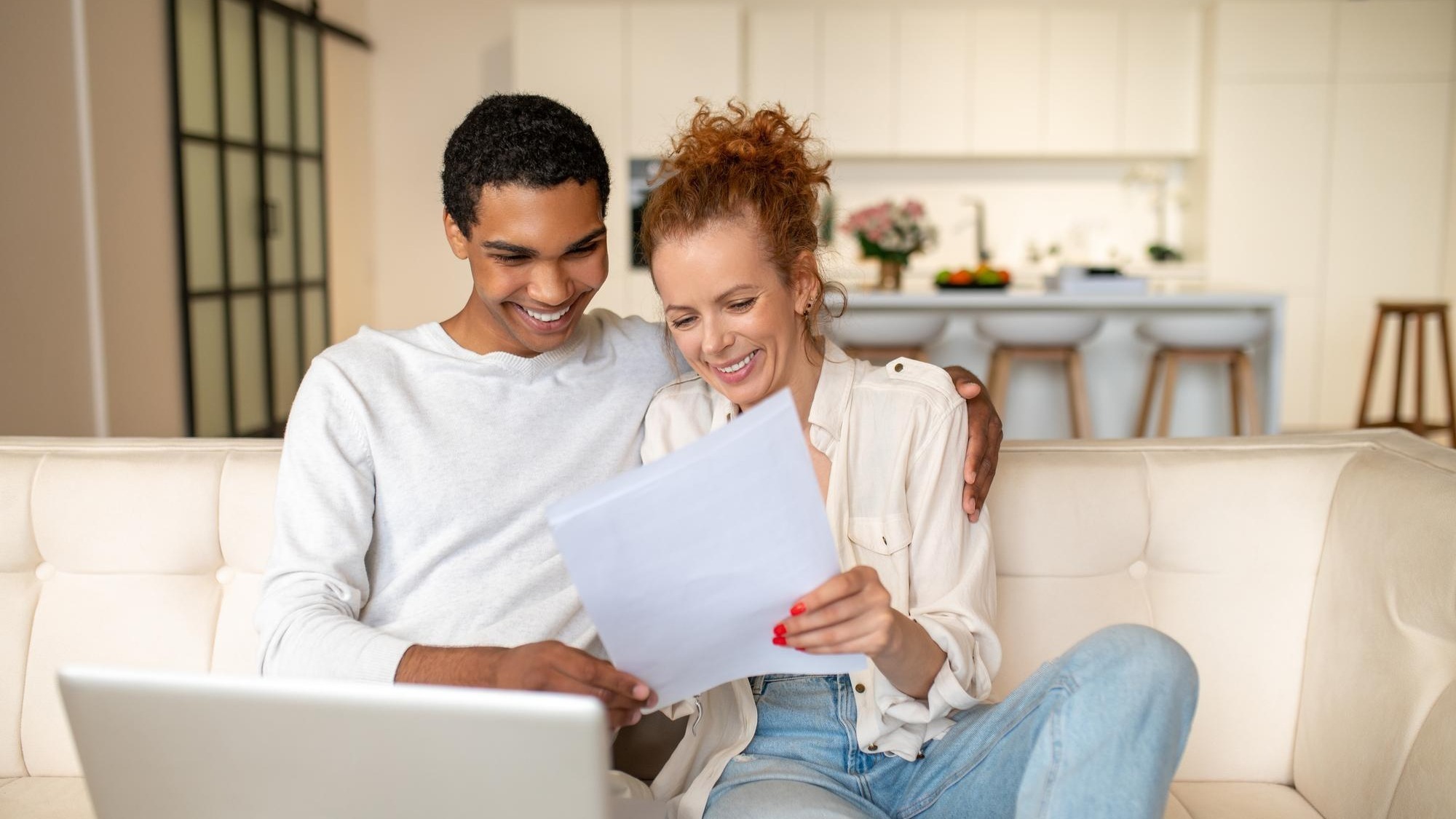 Surfing internet. Young man with a laptop sitting on the sofa, his wife standing next to him