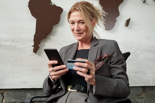 Content mature businesswoman sitting in chair and using smartphone and credit card while transferring money online