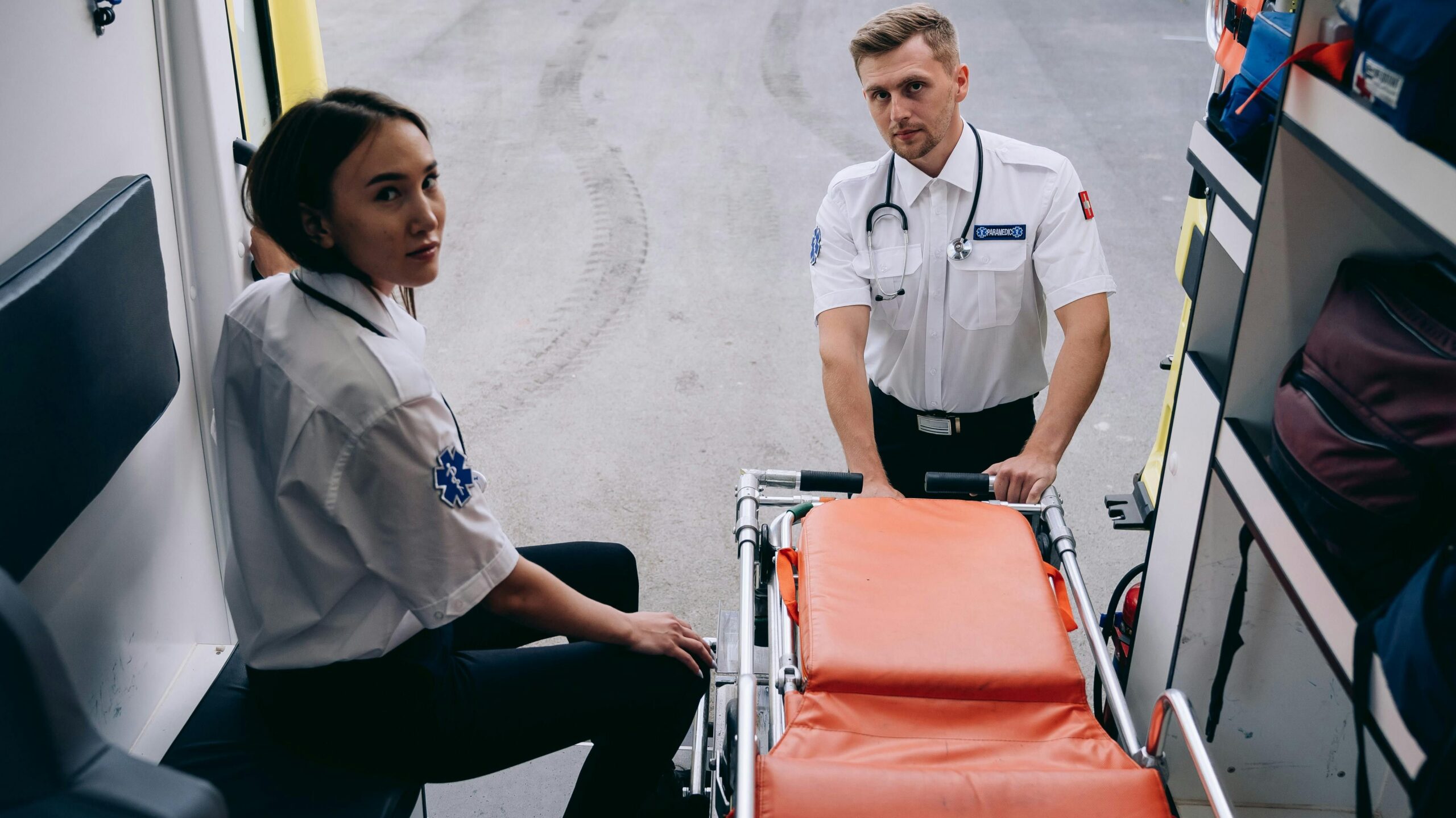 Two paramedics prepare a stretcher inside an ambulance, ready for an emergency response.