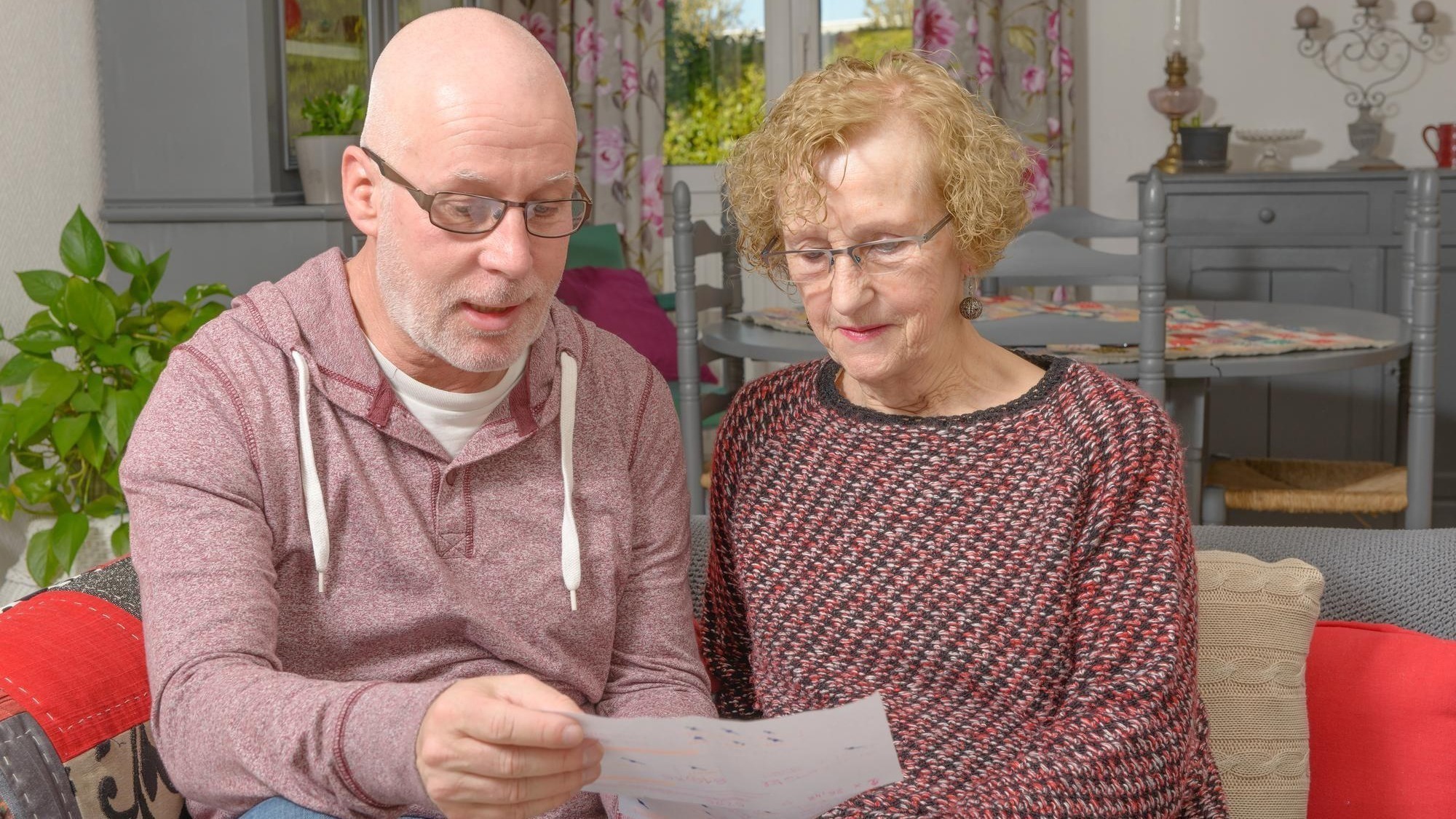 Mature man with woman holding paper on sofa at home