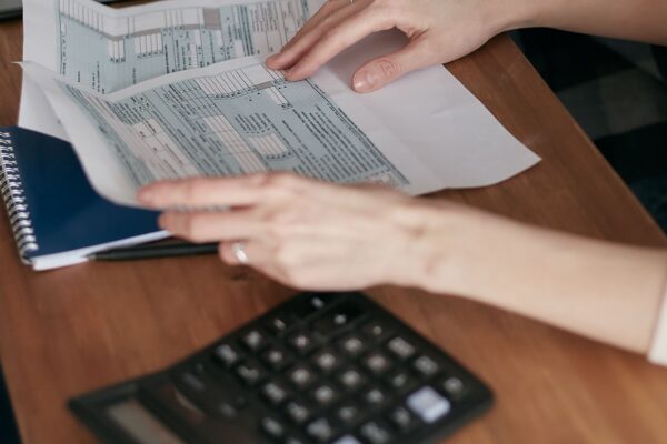 Close-up of hands organizing tax forms on a desk with a calculator, laptop, and notebook.