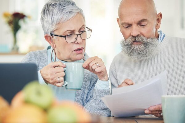 Laptop senior couple and finance documents in home for budget savings or taxes in house Computer retirement and man and woman with paperwork for financial planning insurance or bills with coffee